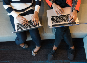 An overhead photo of two people sitting next two each other on a couch, working on laptops